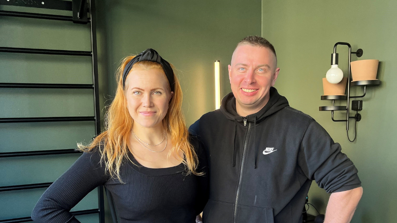 Kuvassa Palauttamon yrittäjät Jenna Lempinen ja Joni Häikiö seisovat vierekkäin vihreän seinän edessä. Jenna Lempisellä on vaaleat hiukset ja musta panta, ja hänellä on yllään musta paita. Joni Häikiöllä on musta huppari, jossa on Nike-logo. Taustalla näkyy moderni seinävalaisin.